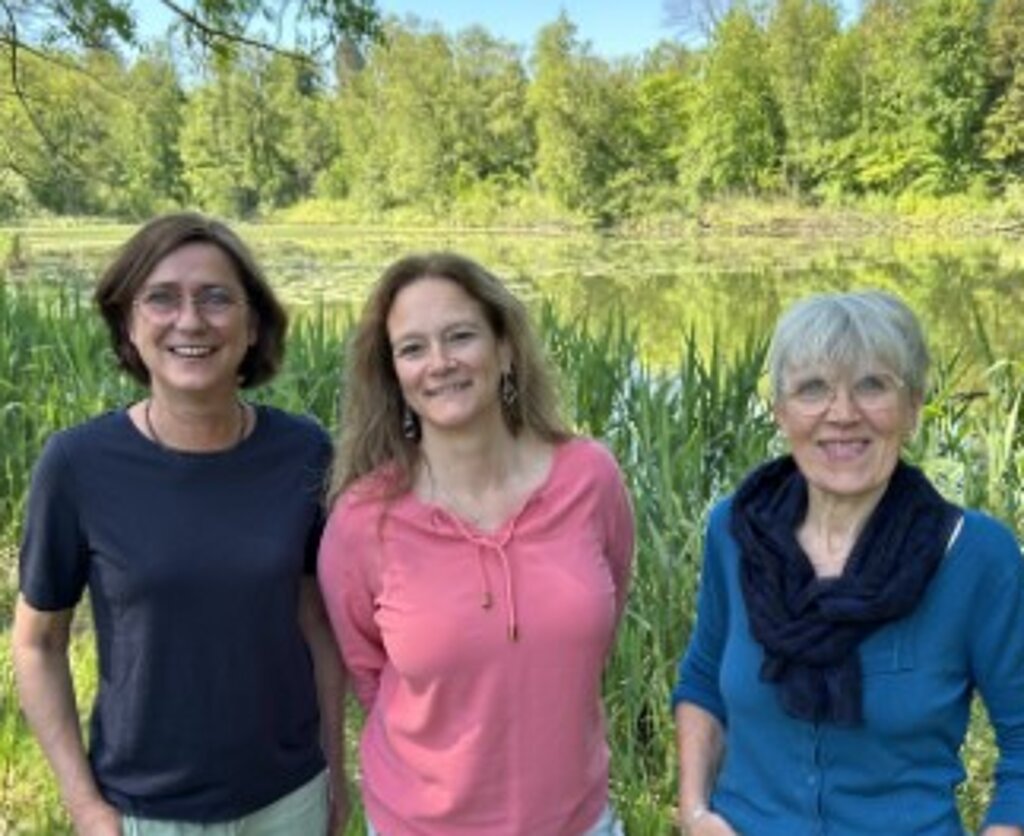 Auf dem Bild sind 3 lächelnde Frauen vor strahlend grüner Natur zu sehen