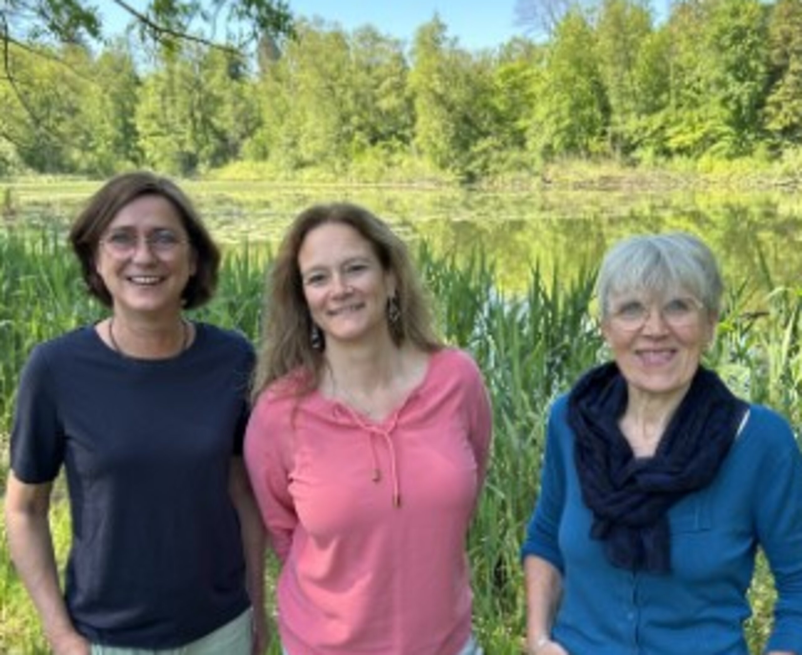 Auf dem Bild sind 3 lächelnde Frauen vor strahlend grüner Natur zu sehen
