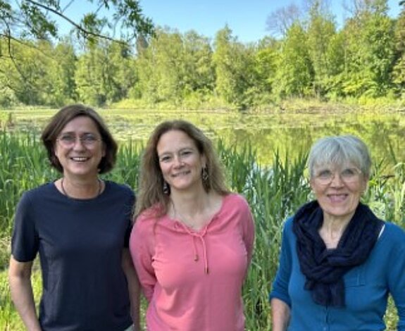 Auf dem Bild sind 3 lächelnde Frauen vor strahlend grüner Natur zu sehen