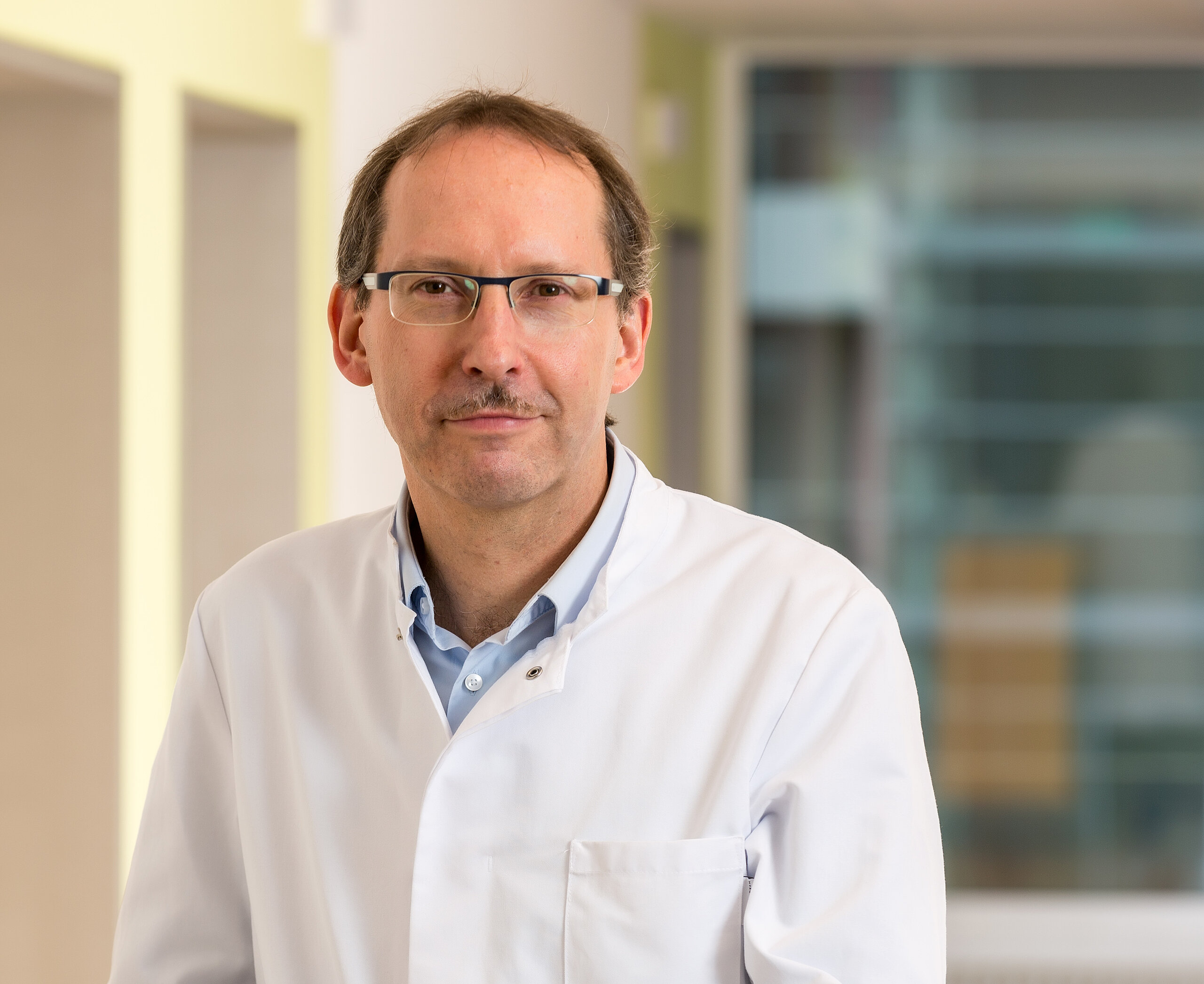 Dr. Klaus Müller, Chefarzt der Klinik im Hofgarten, steht an einem Stationswagen und lächelt freundlich