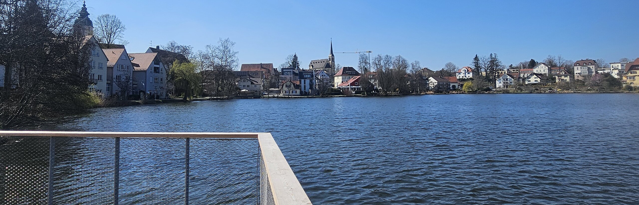 Holzsteg führt in den Stadtsee von Bad Waldsee, unter strahlend blauem Himmel.