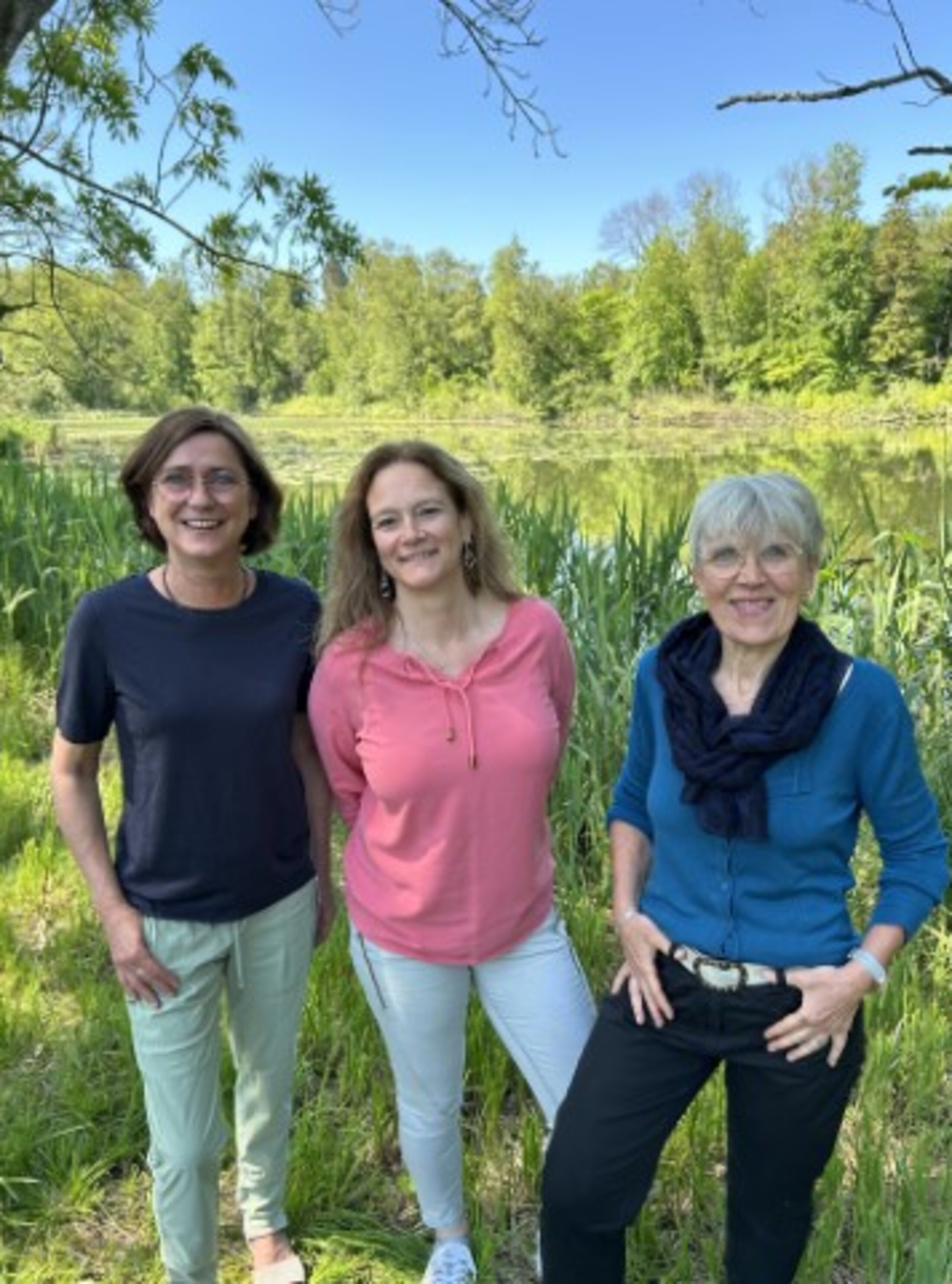 Auf dem Bild sind 3 lächelnde Frauen vor strahlend grüner Natur zu sehen
